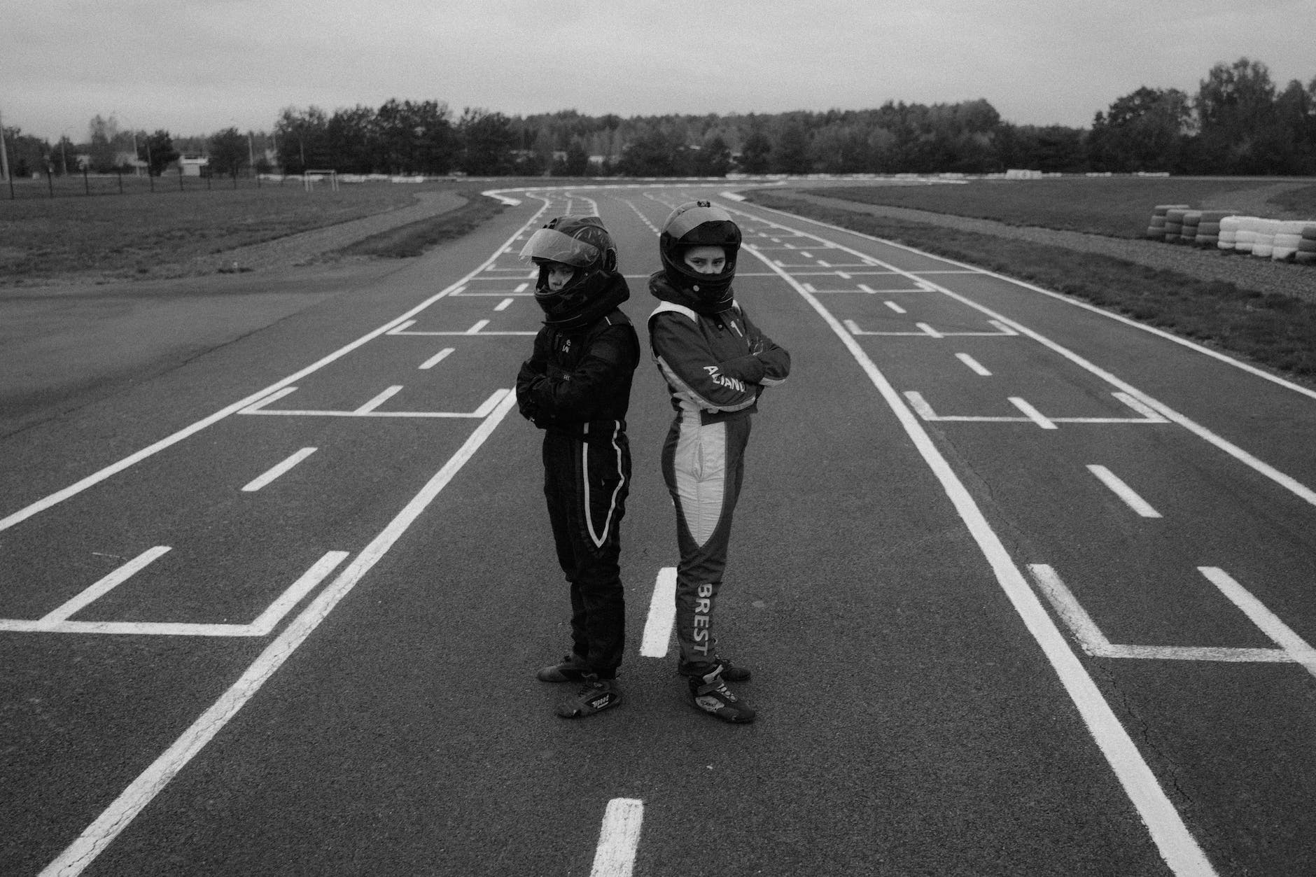 monochrome photo of two athletes in racing suit standing in racetrack