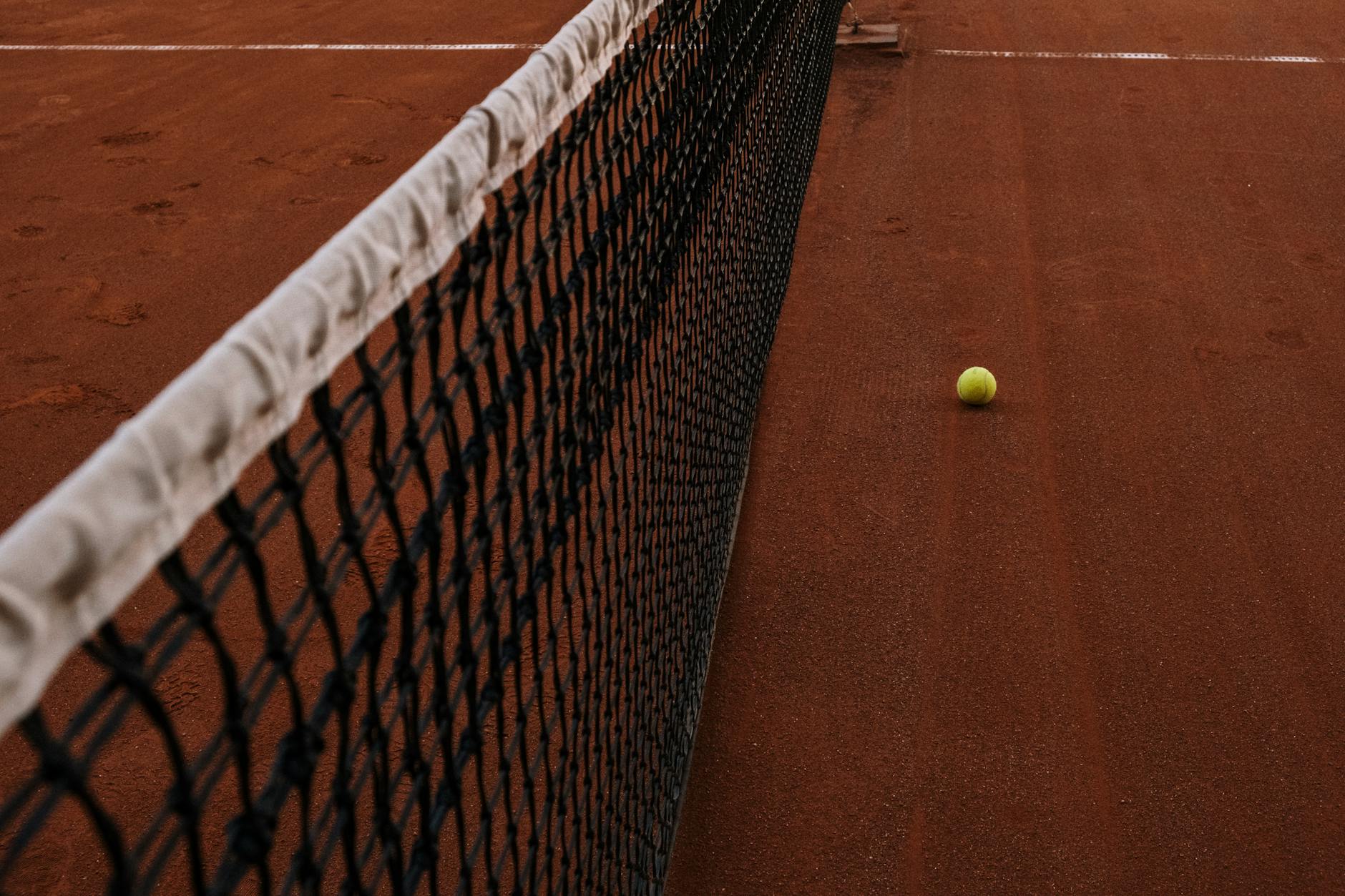 yellow tennis ball lying on clay court by net